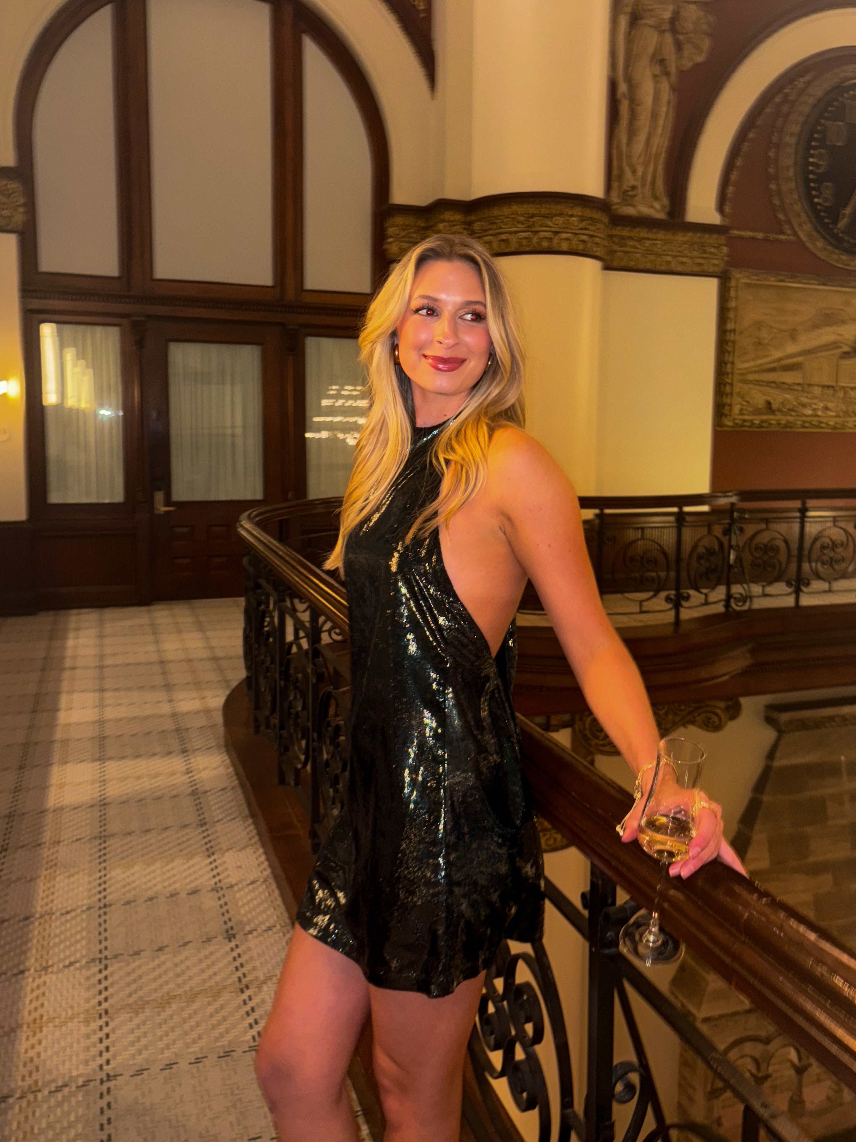 Woman in a green dress holding a glass of white wine in an elegant interior setting.