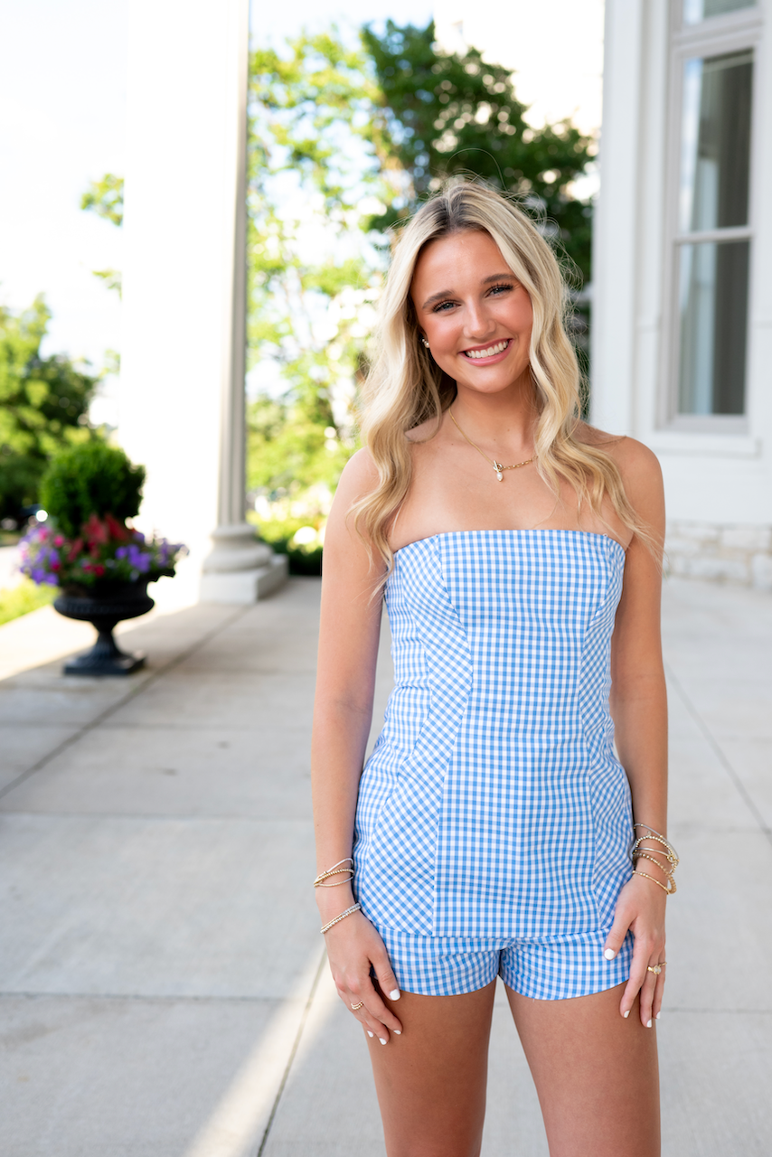Woman wearing a blue checkered strapless romper standing outdoors.