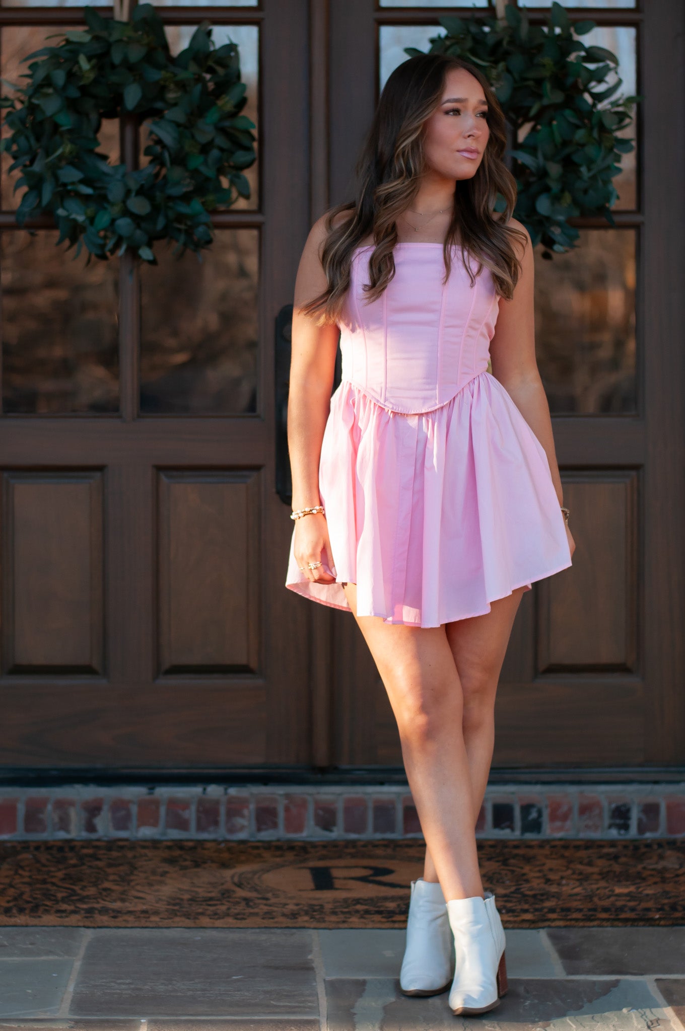 Woman wearing pink strapless mini dress standing in front of wooden doors