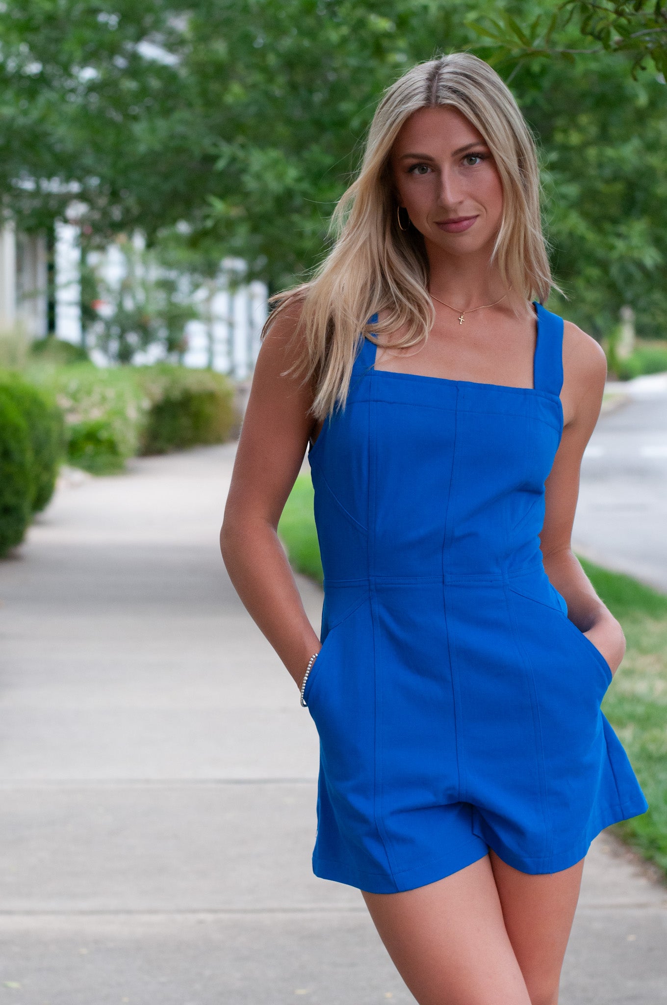 Woman in a blue romper standing on a path with greenery in the background