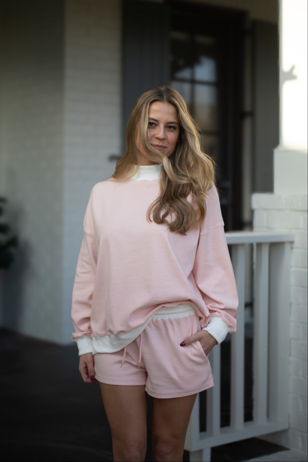 Woman wearing a pink outfit standing on a porch.