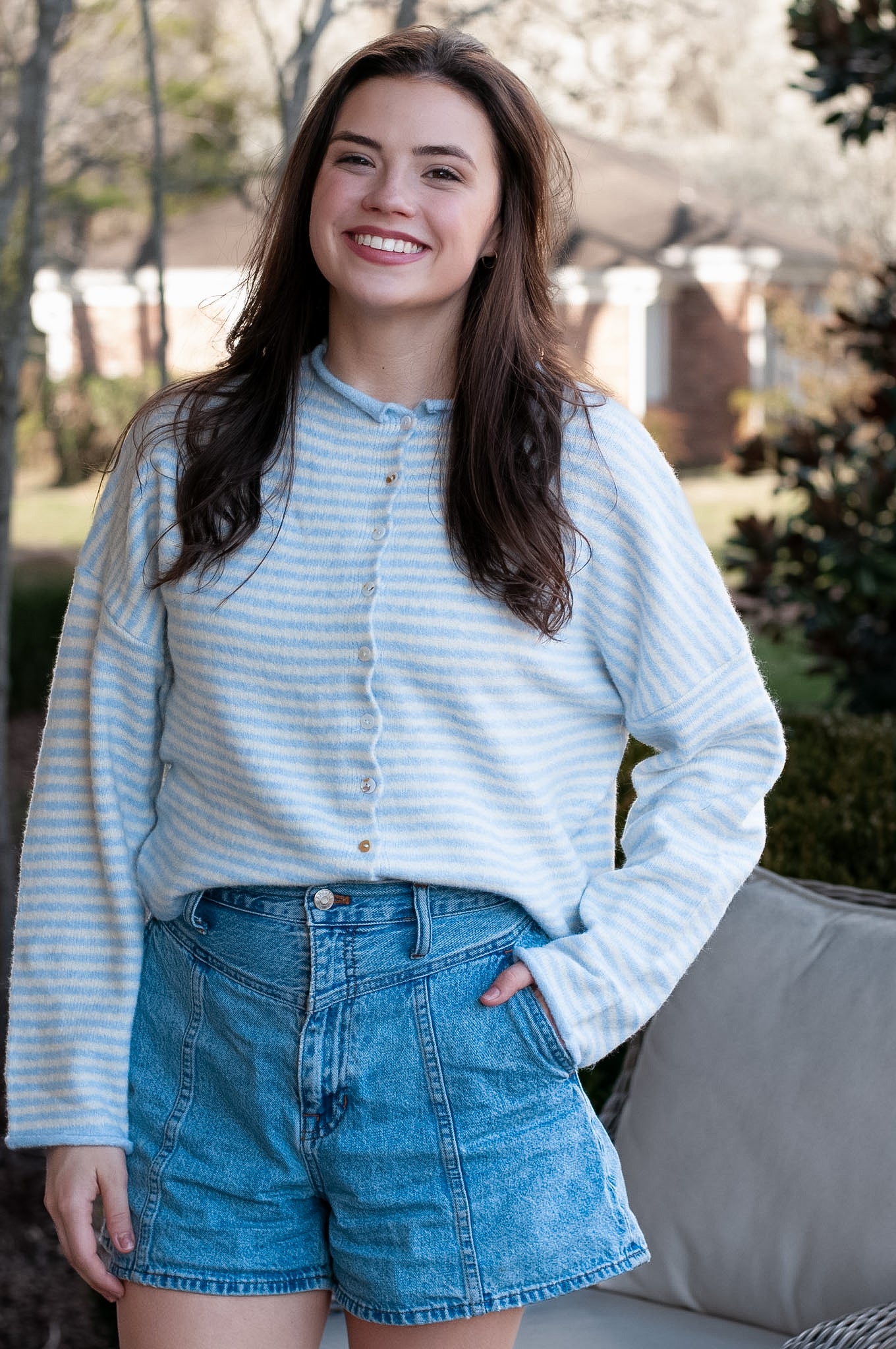 Woman wearing a light blue striped shirt and denim shorts outdoors.