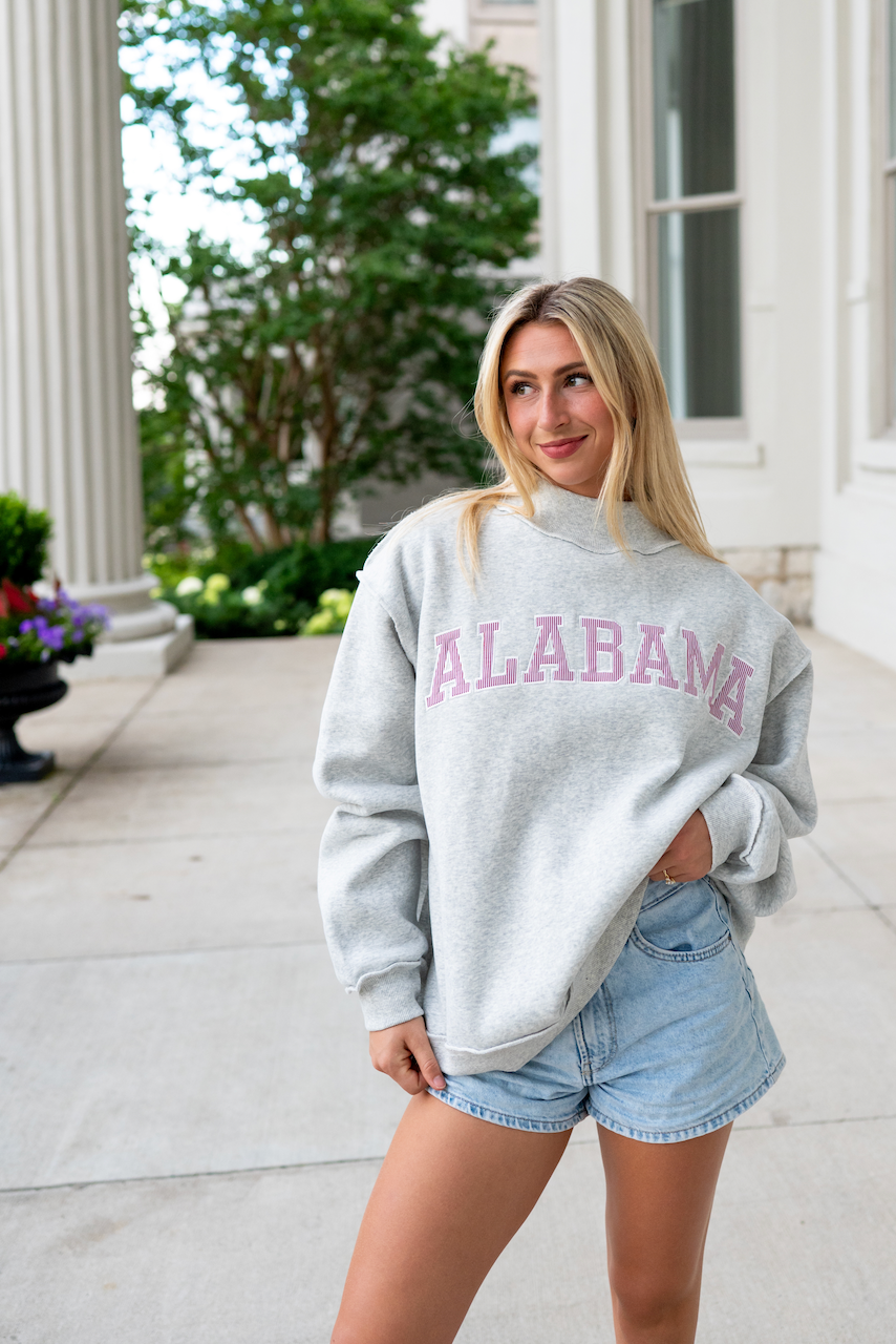 Woman wearing a gray sweatshirt with 'Alabama' printed on it, standing outdoors.