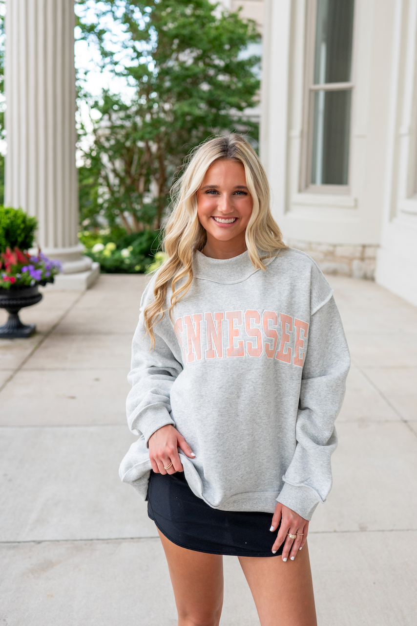 Woman wearing a gray sweatshirt with 'Tennessee' printed on it, standing outdoors.