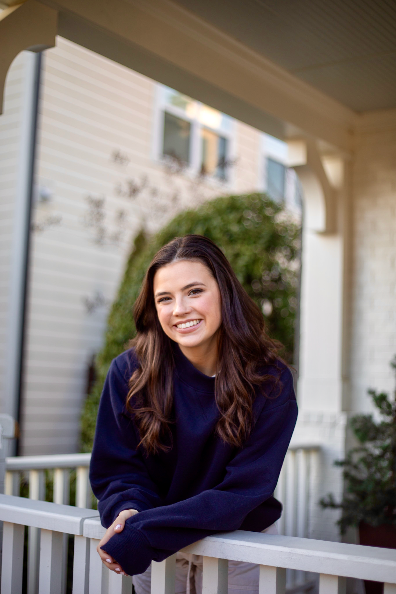 Lady wearing navy sweatshirt leaning on railing of white porch