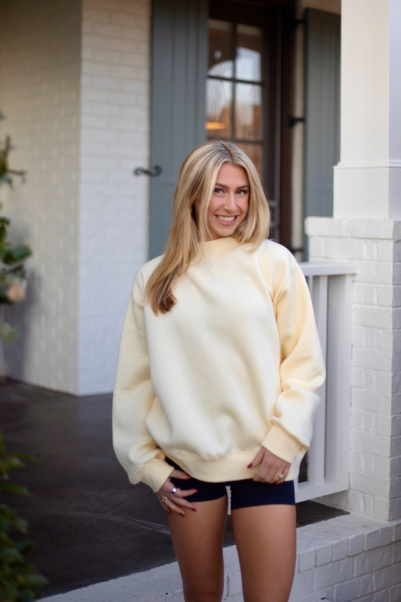 Lady wearing yellow sweatshirt standing in front of white porch