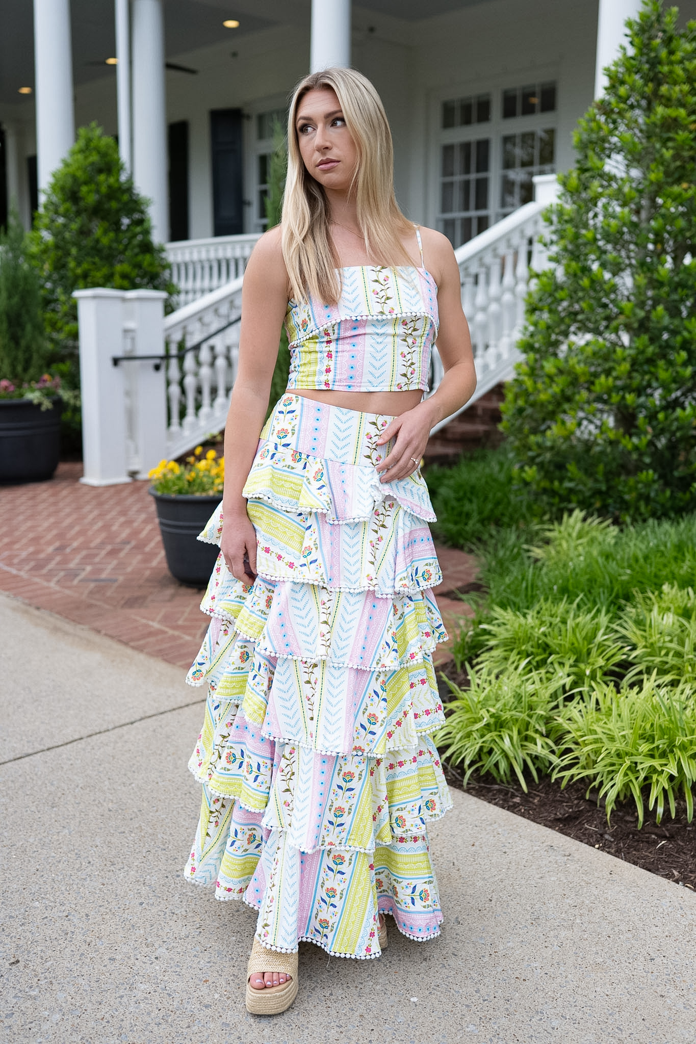 Woman wearing a colorful patterned dress standing outdoors near a house.