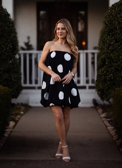 Woman in a black strapless dress with white polka dots walking outdoors.