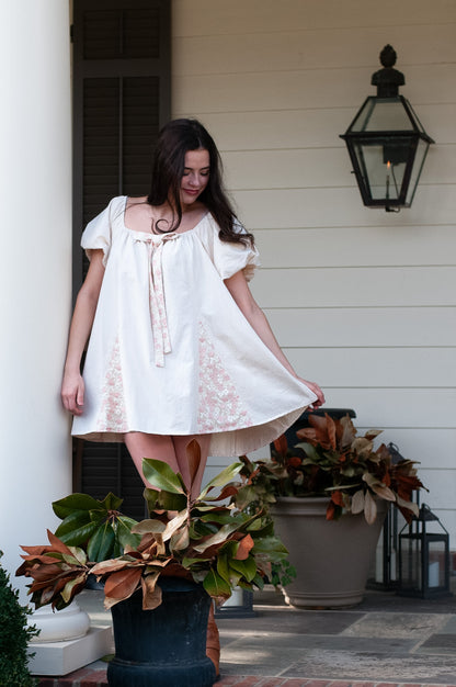 Woman in a white dress standing on a porch with decorative plants and lanterns.