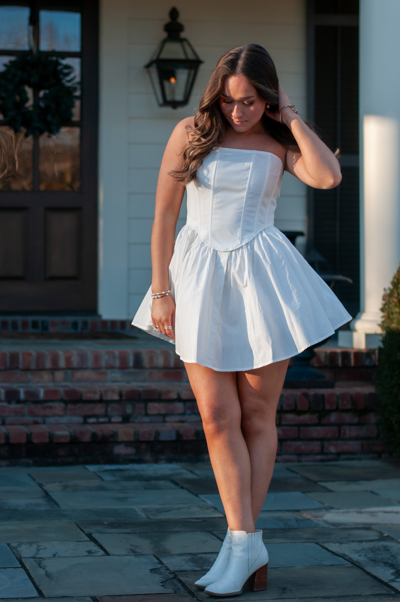 Woman wearing white strapless mini dress in front of brick steps