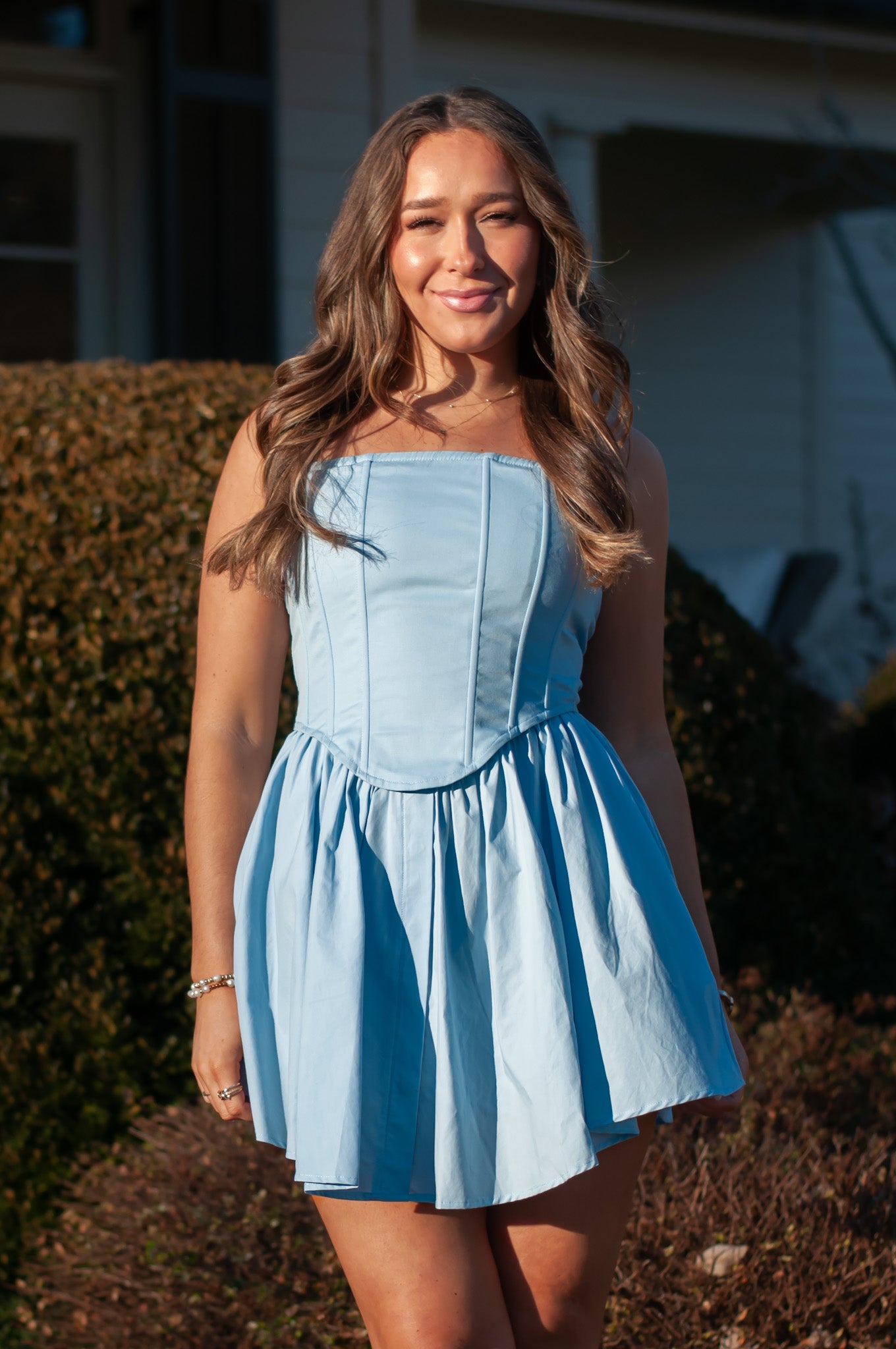 Woman wearing blue mini dress standing in front of brown bushes