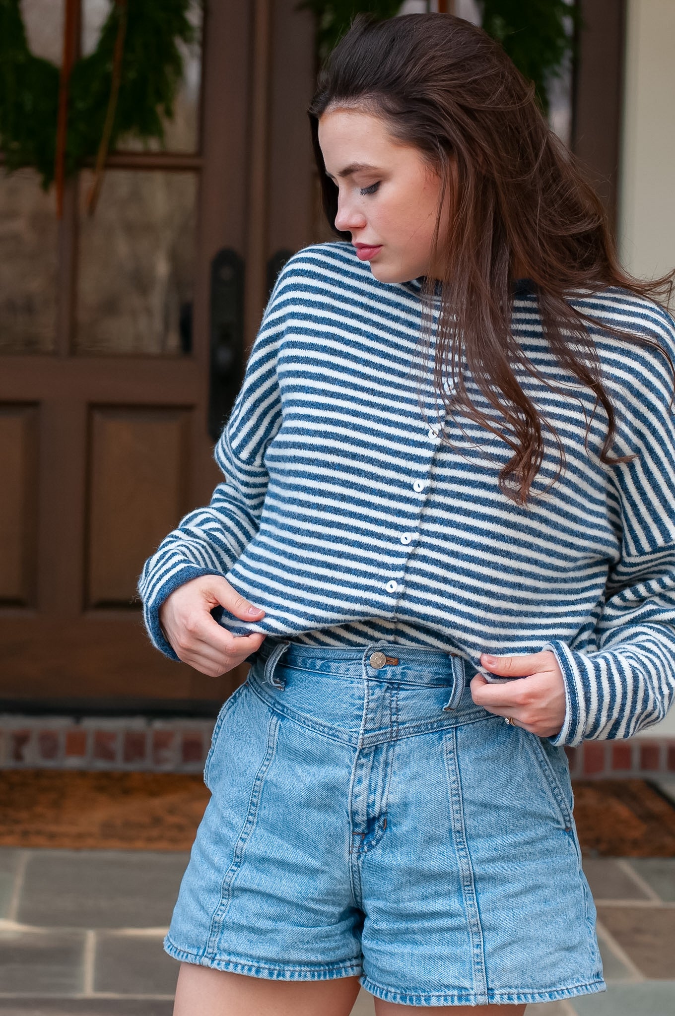 Woman wearing a striped shirt and denim shorts standing outdoors.