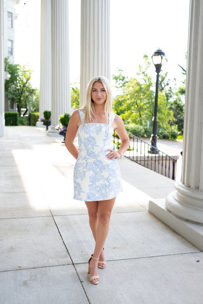 Woman in a light blue floral dress standing in front of classical columns.