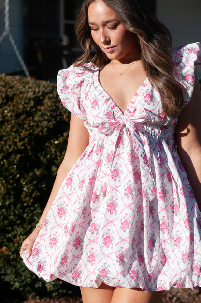 Woman wearing pink and white bubble mini dress standing in front of green bush