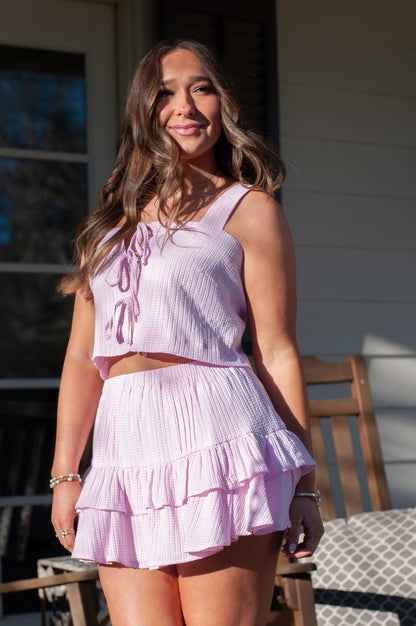 Woman wearing pink gingham mini skirt set standing on white porch