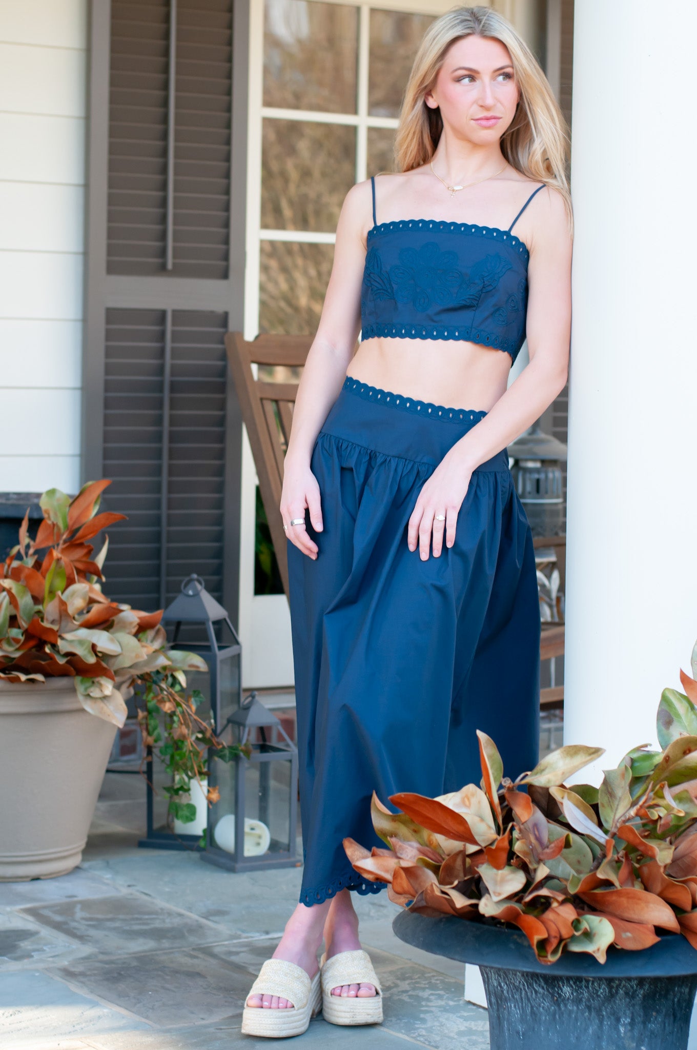Woman in a blue dress standing on a porch with potted plants.