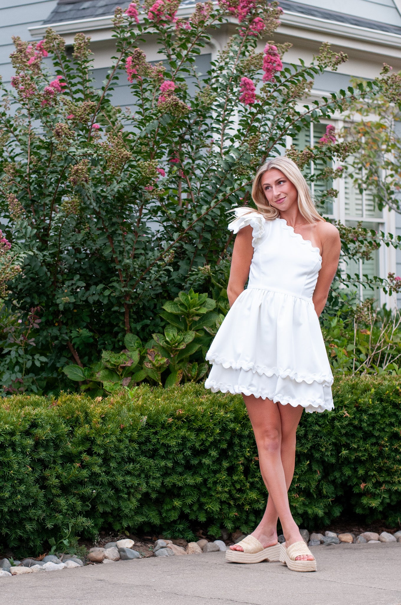 Woman in a white dress standing outdoors with greenery and flowers in the background