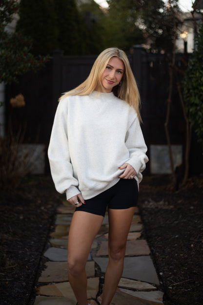 Woman wearing a white sweatshirt and black shorts standing outdoors.