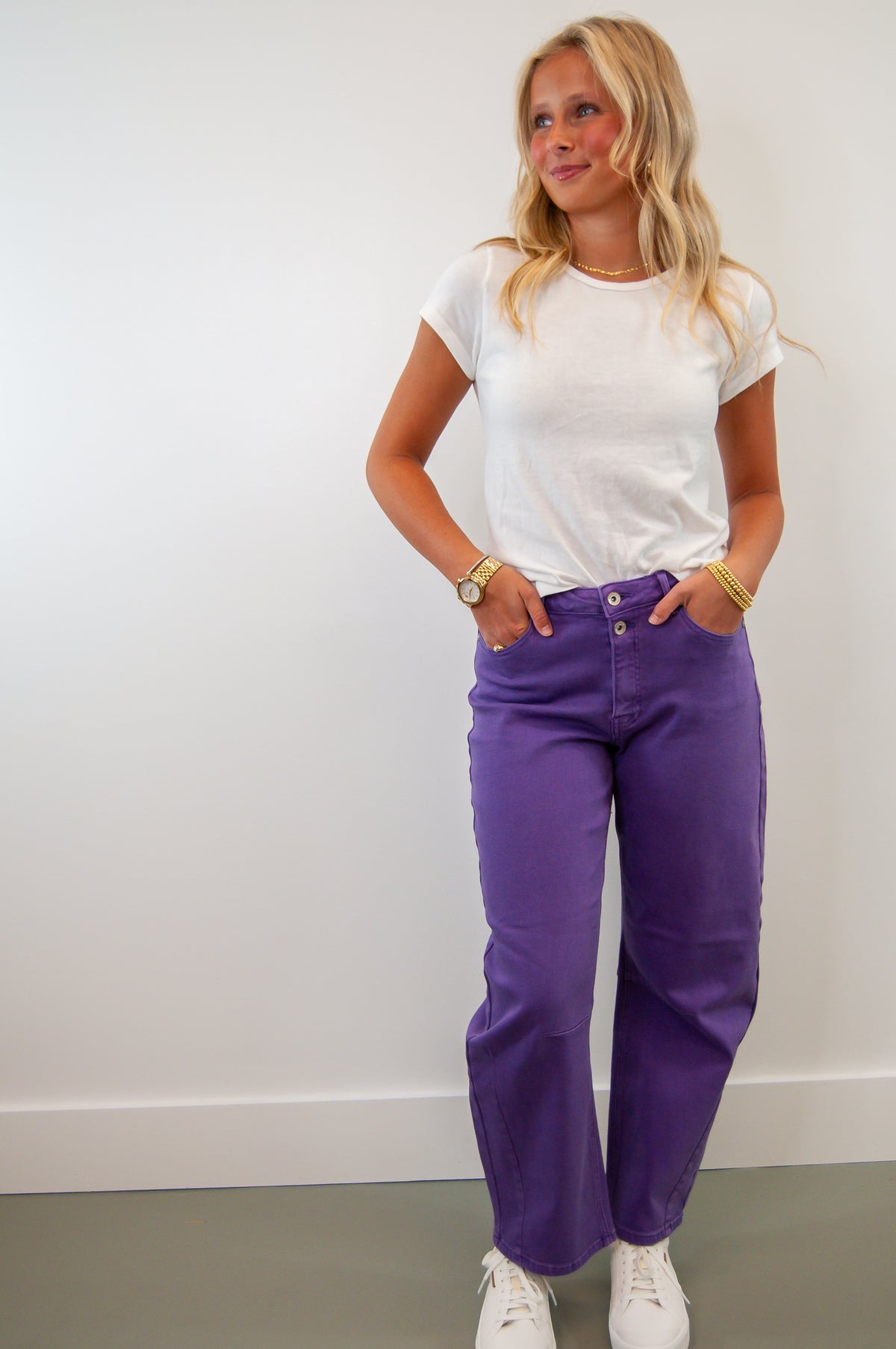 A person wearing a white t-shirt and purple high waist stretch barrel jeans, standing against a plain background.