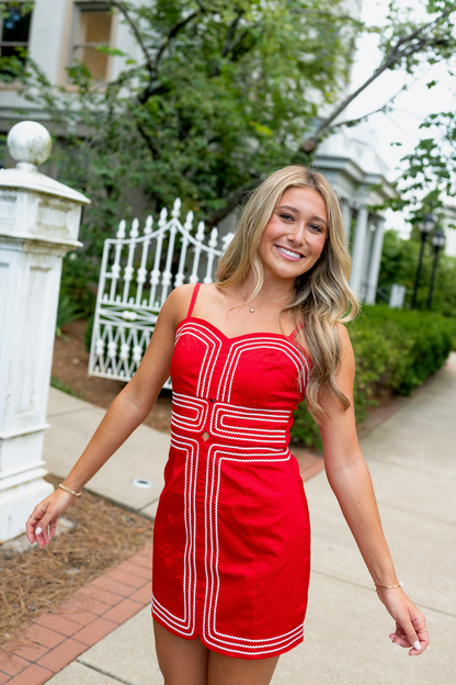 Woman in a red dress standing outdoors with greenery and a white fence in the background