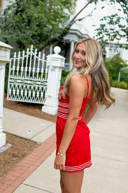 Woman in a red dress standing on a sidewalk with a white fence and trees in the background