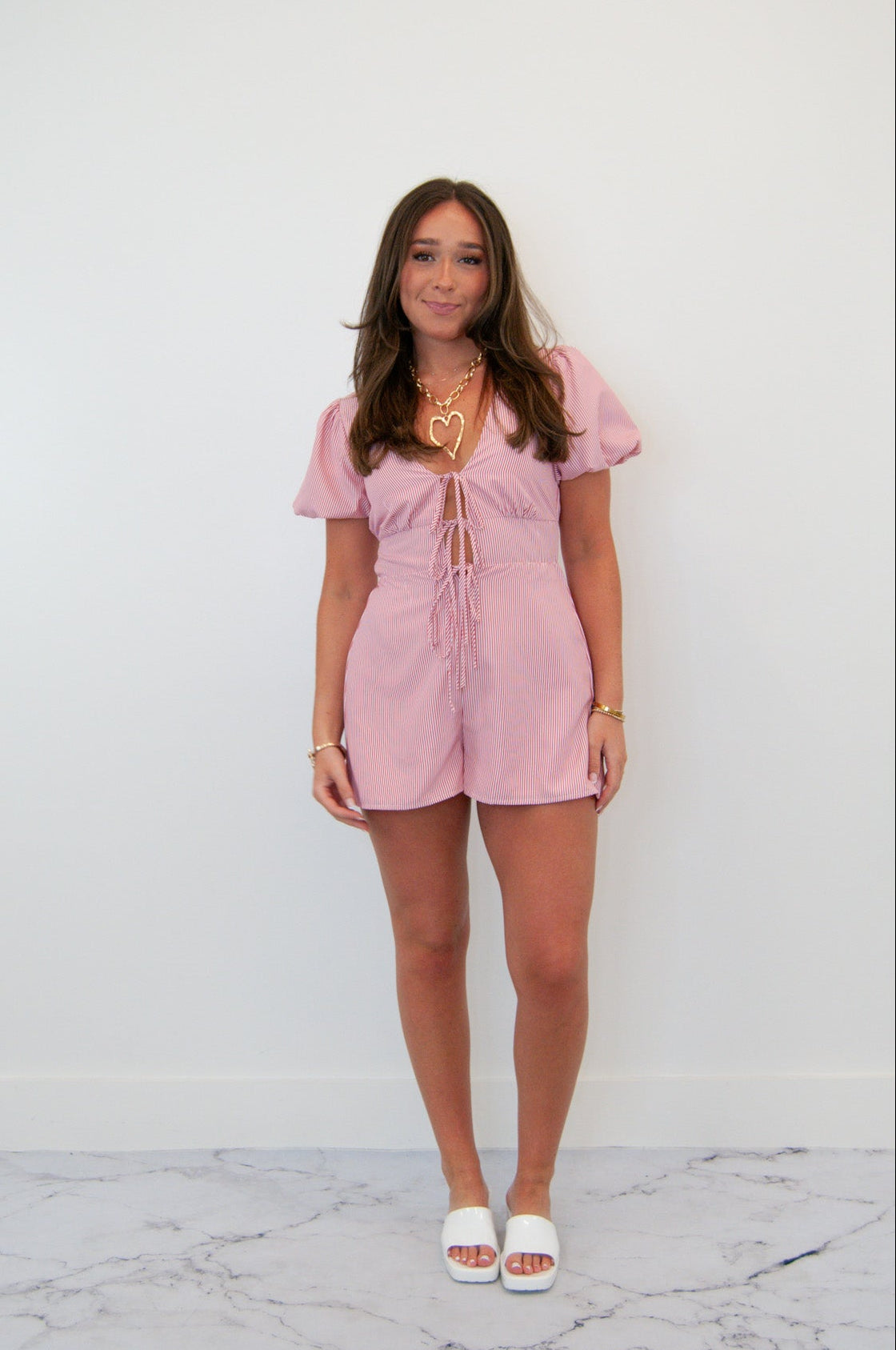 A woman standing in front of a white background wearing a red plunge tie front romper with bubble sleeves.