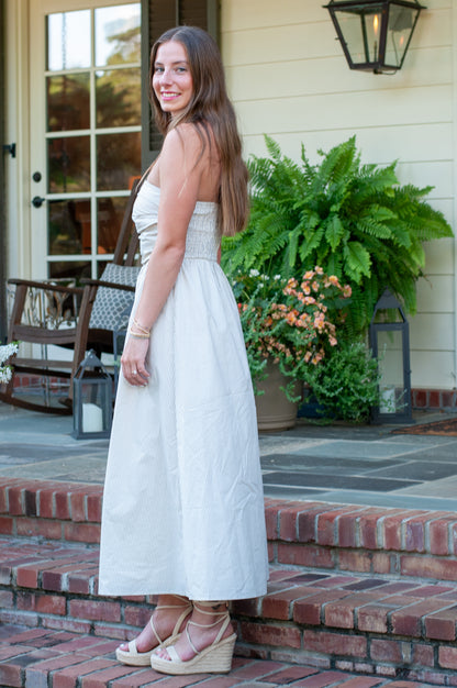 Woman in a white dress standing on a porch with plants and furniture in the background