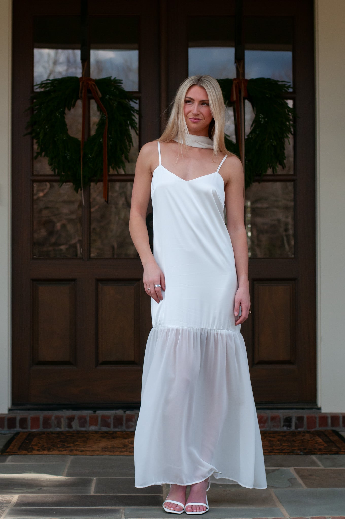 Woman in a white slip dress standing in front of a wooden door with wreaths.