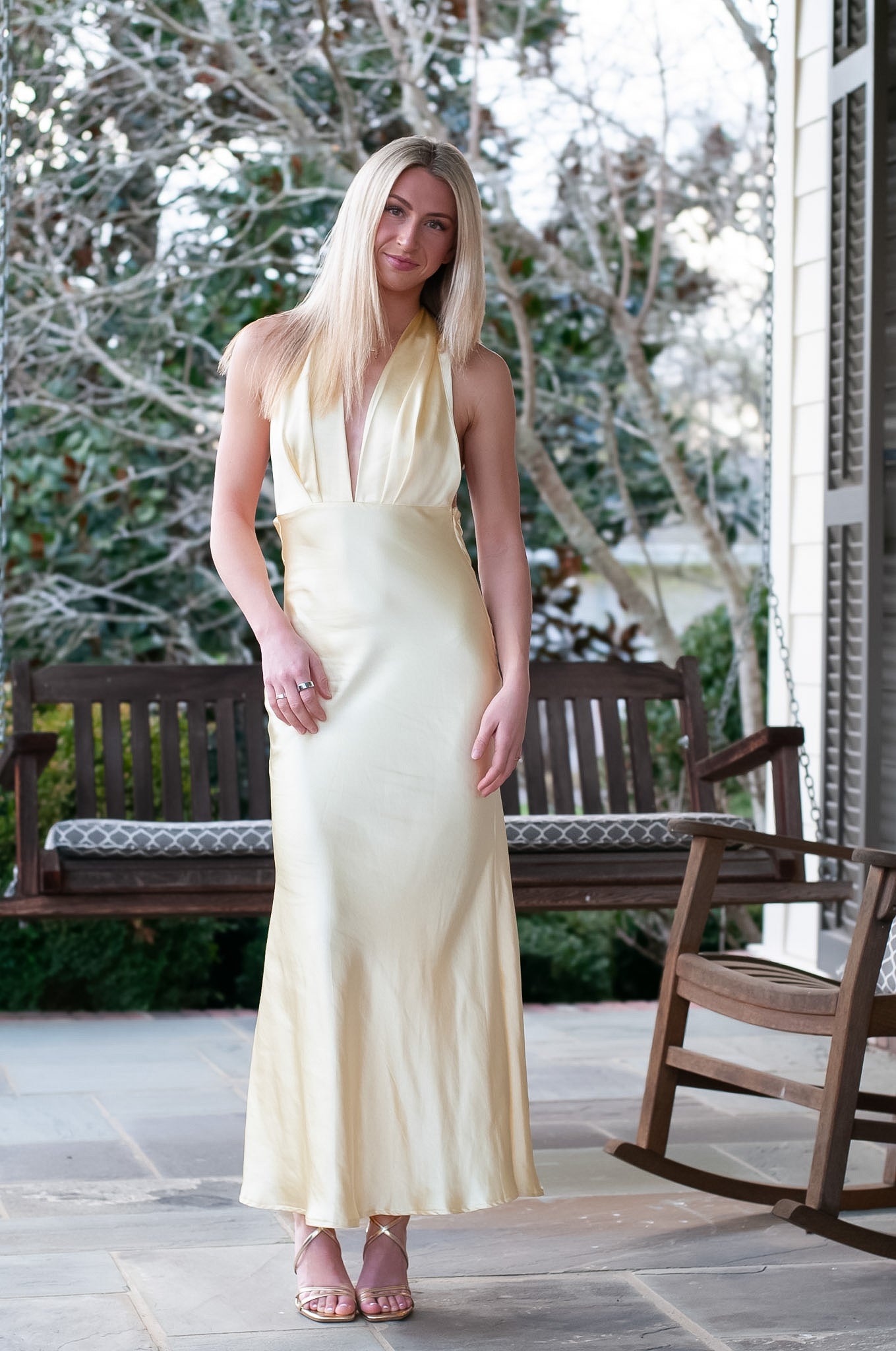 Woman in a long light yellow dress standing outdoors with trees in the background