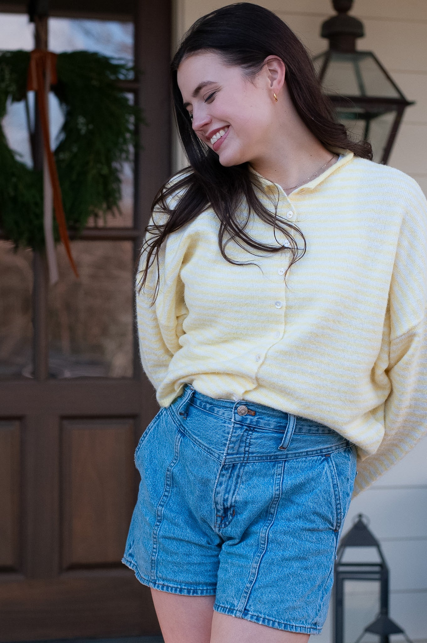 Woman wearing a yellow sweater and blue shorts standing outdoors.