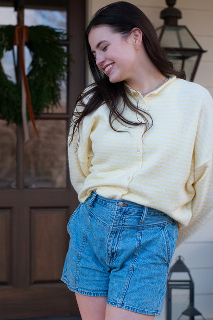 Woman wearing a yellow sweater and blue shorts standing outdoors.