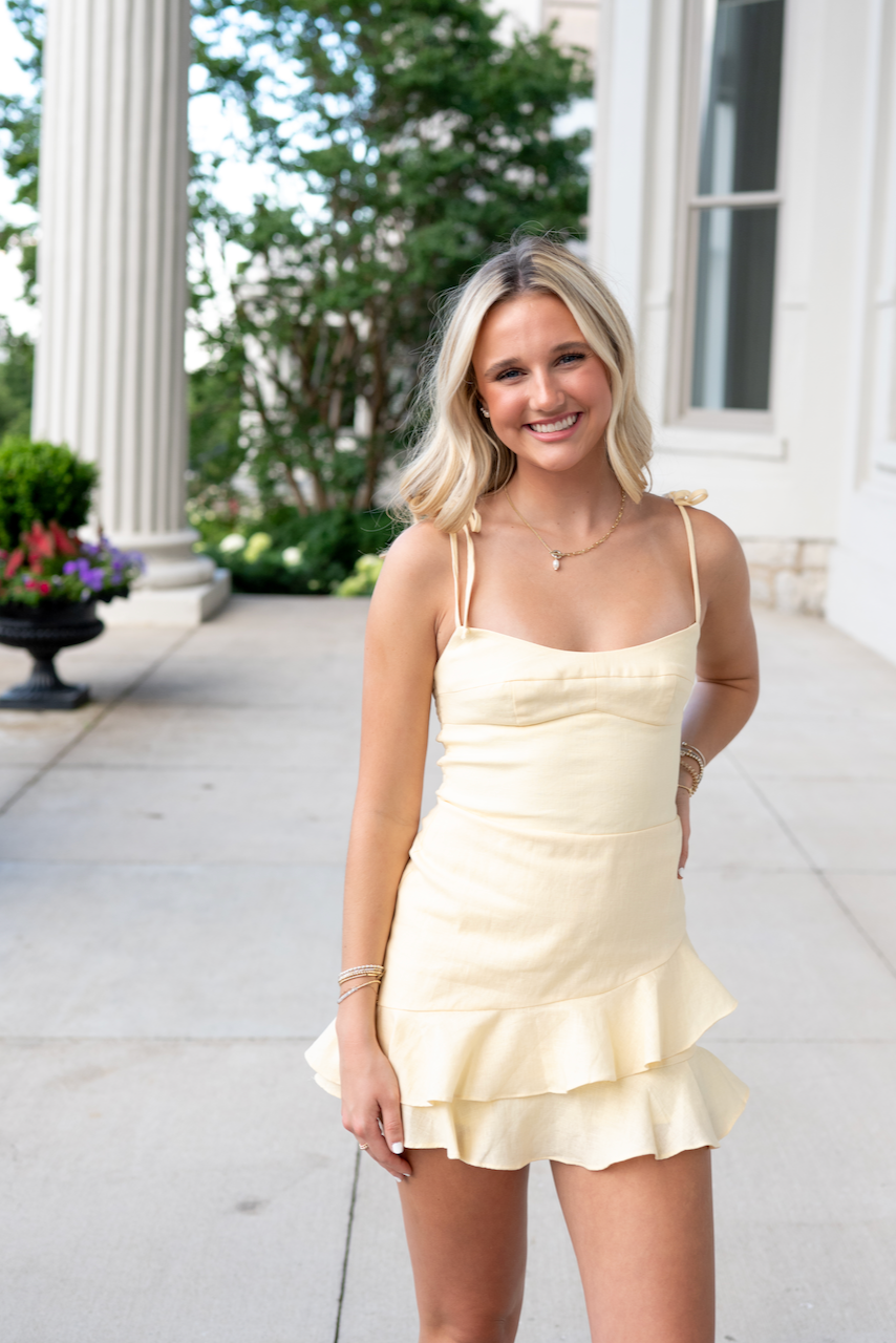Woman in a light yellow dress standing outdoors with classical architecture in the background