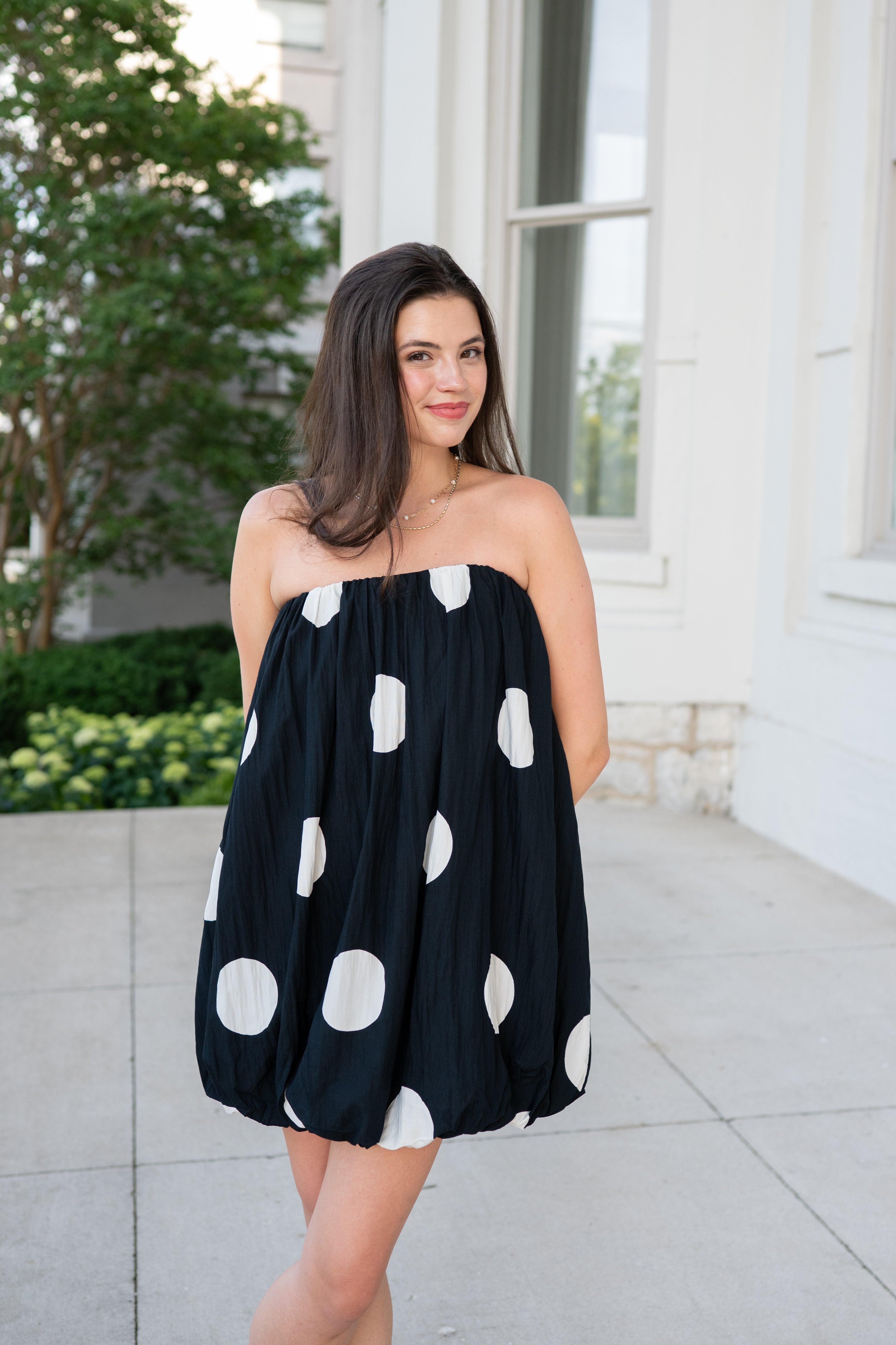 Woman wearing a black strapless dress with white polka dots standing outdoors.